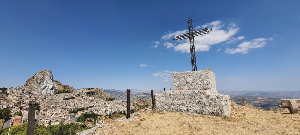 Una croce posta a strapiombo sul monte e a sinistra Caltabellotta 